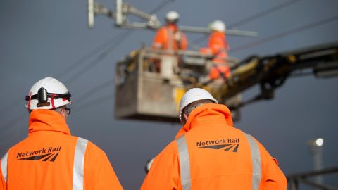 Engineers wearing Network Rail branded orange jackets work on overhead wires