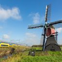 A typical yellow-blue NS train passing a windmill in the Netherlands