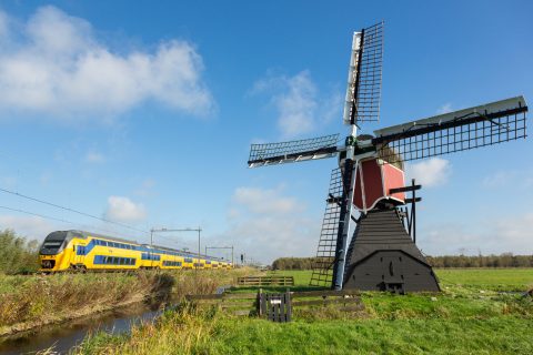 A typical yellow-blue NS train passing a windmill in the Netherlands