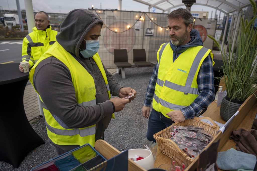 Infrabel-medewerker reikt geurverfrisser uit aan vrachtwagenchaufferus bij de Combinant terminal in Antwerpen 